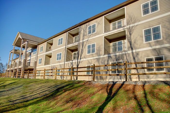 A residential apartment building with balconies and a wooden fence, set against a clear sky.
