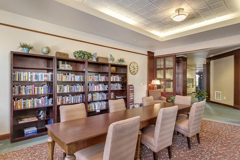 A cozy library space with a wooden table, chairs, and bookshelves filled with books.