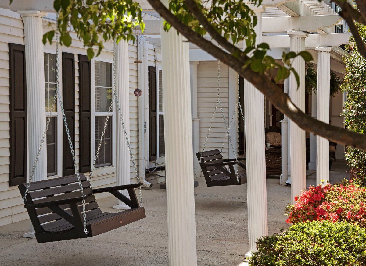 A charming porch with swings, white columns, and lush greenery.
