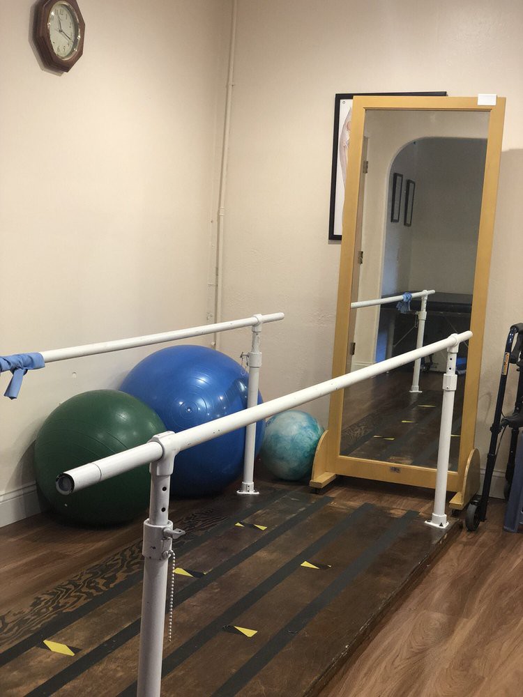 A physical therapy room equipped with parallel bars, exercise balls, and a mirror.