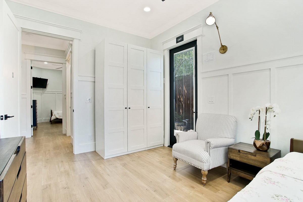 A modern living room with a cozy armchair, wood flooring, and elegant white walls accented by a stylish lighting fixture.