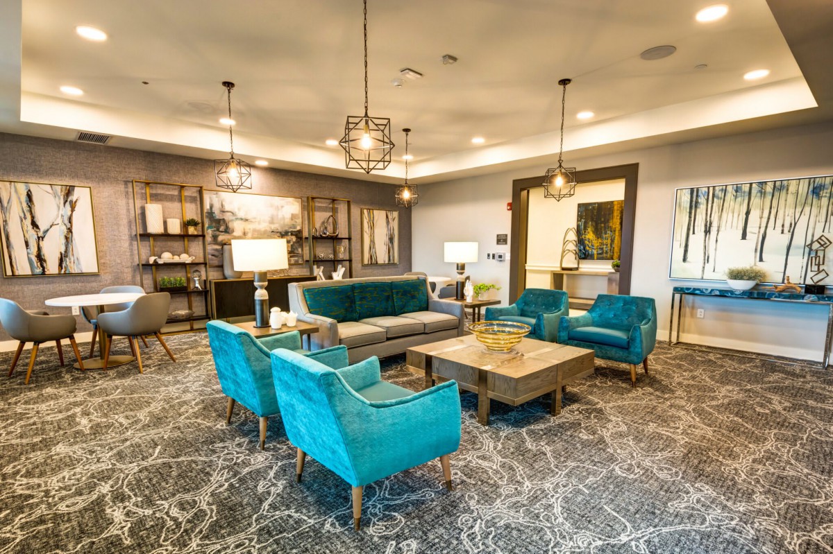 A stylish modern living room features teal chairs and a sofa, complemented by elegant chandeliers and a patterned rug.