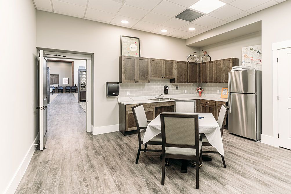 A modern kitchen with a small dining area featuring wood flooring, sleek cabinets, and a stainless steel refrigerator.