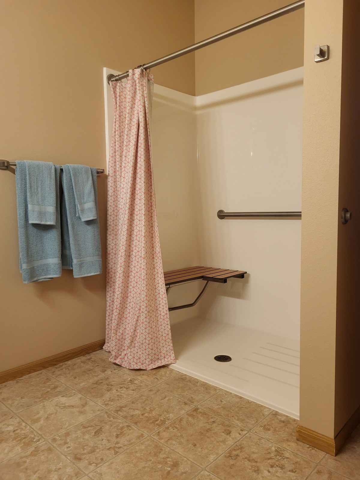 An accessible bathroom with a shower featuring a folding seat and grab bar.