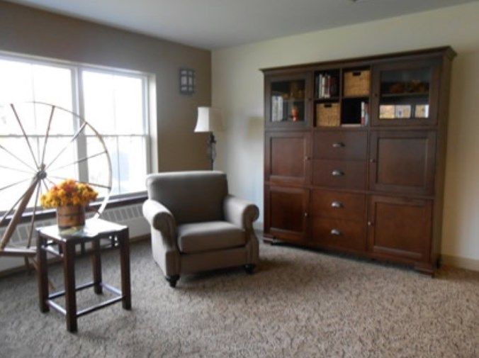 A cozy living room featuring an armchair, large bookshelf, and a window with natural light.