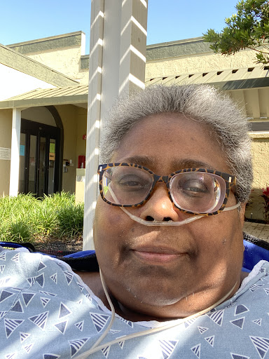 A woman wearing glasses smiles while enjoying the outdoors.