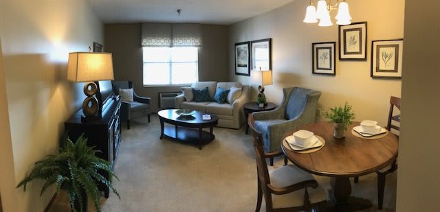 A cozy living room with a sofa, chairs, and a coffee table, featuring warm lighting and neutral tones.