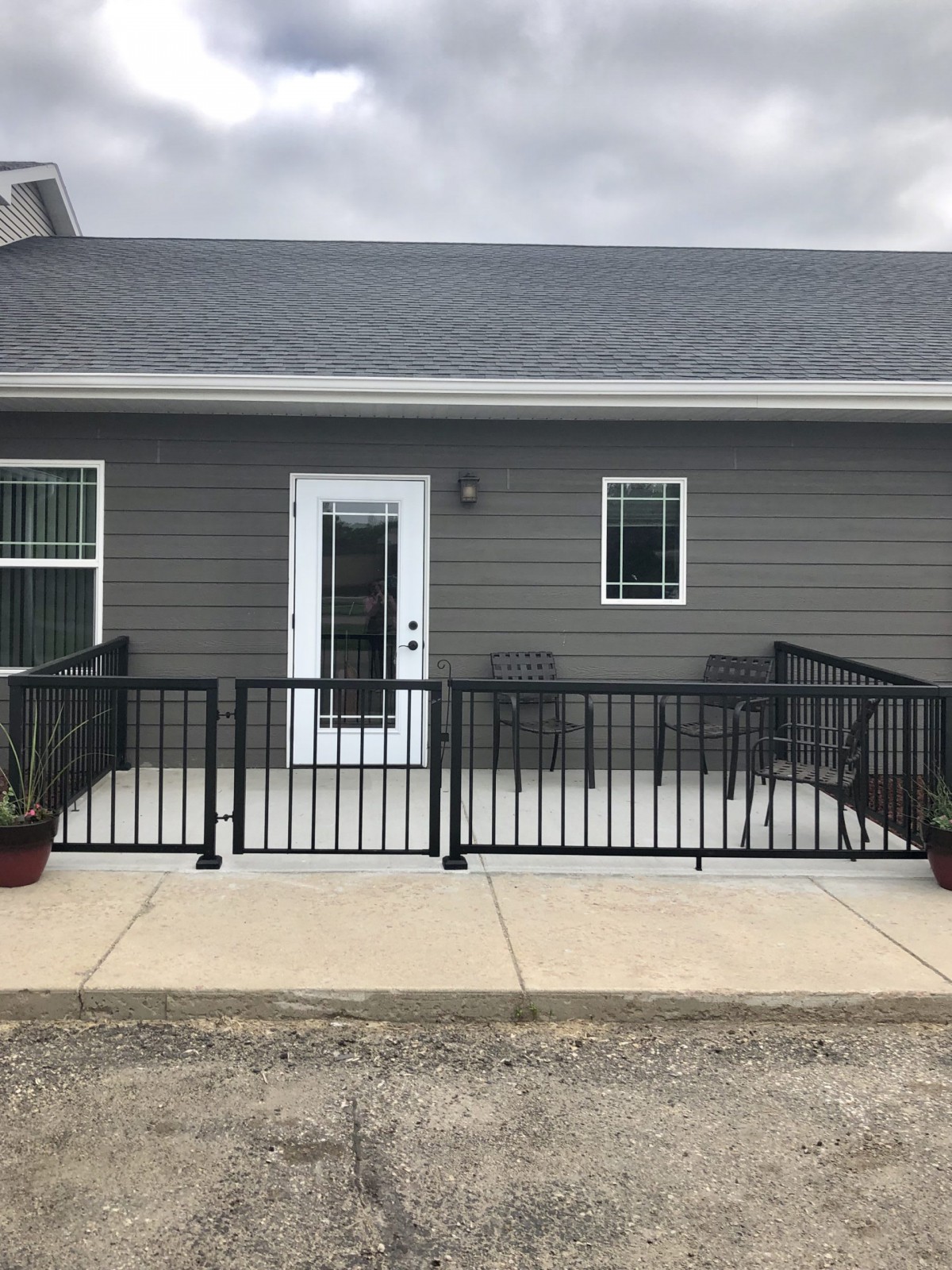 A small house with a porch featuring black railings, plants, and patio furniture.