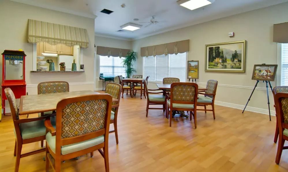 A well-furnished dining area with several tables and chairs, featuring large windows and wood flooring.