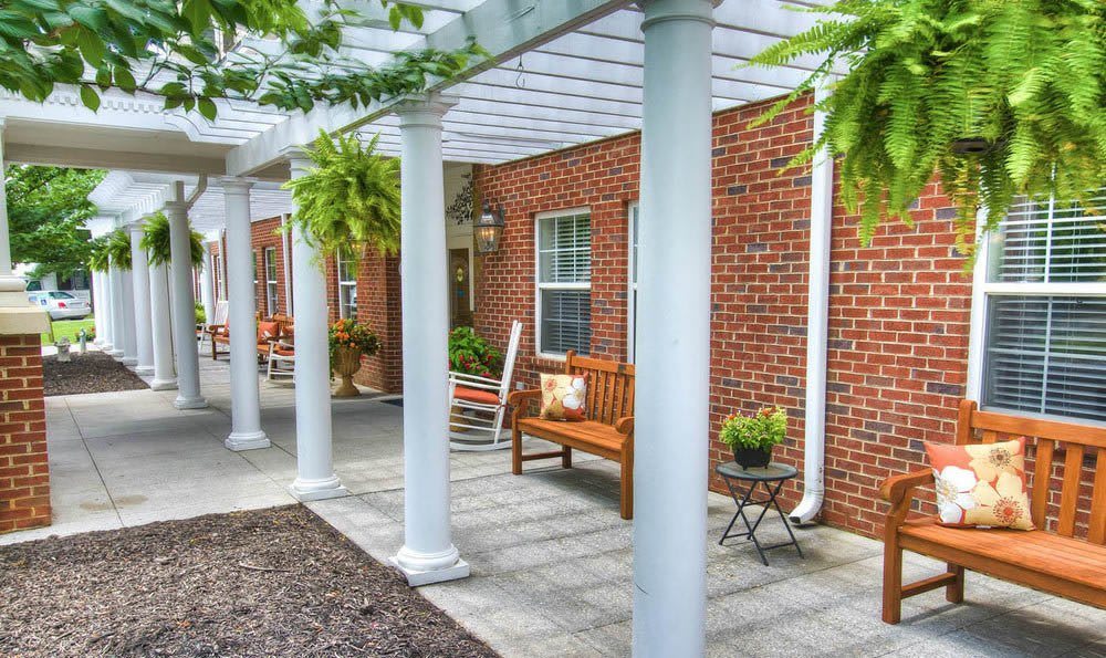 A charming outdoor area featuring a pergola with hanging plants, a wooden bench, and a brick building backdrop.