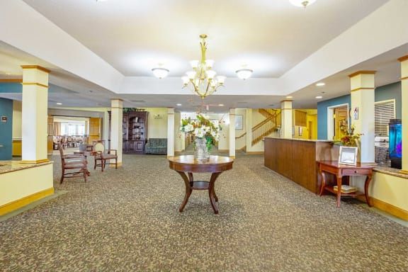 A spacious lobby area with elegant decor, featuring a central table with flowers under a chandelier.