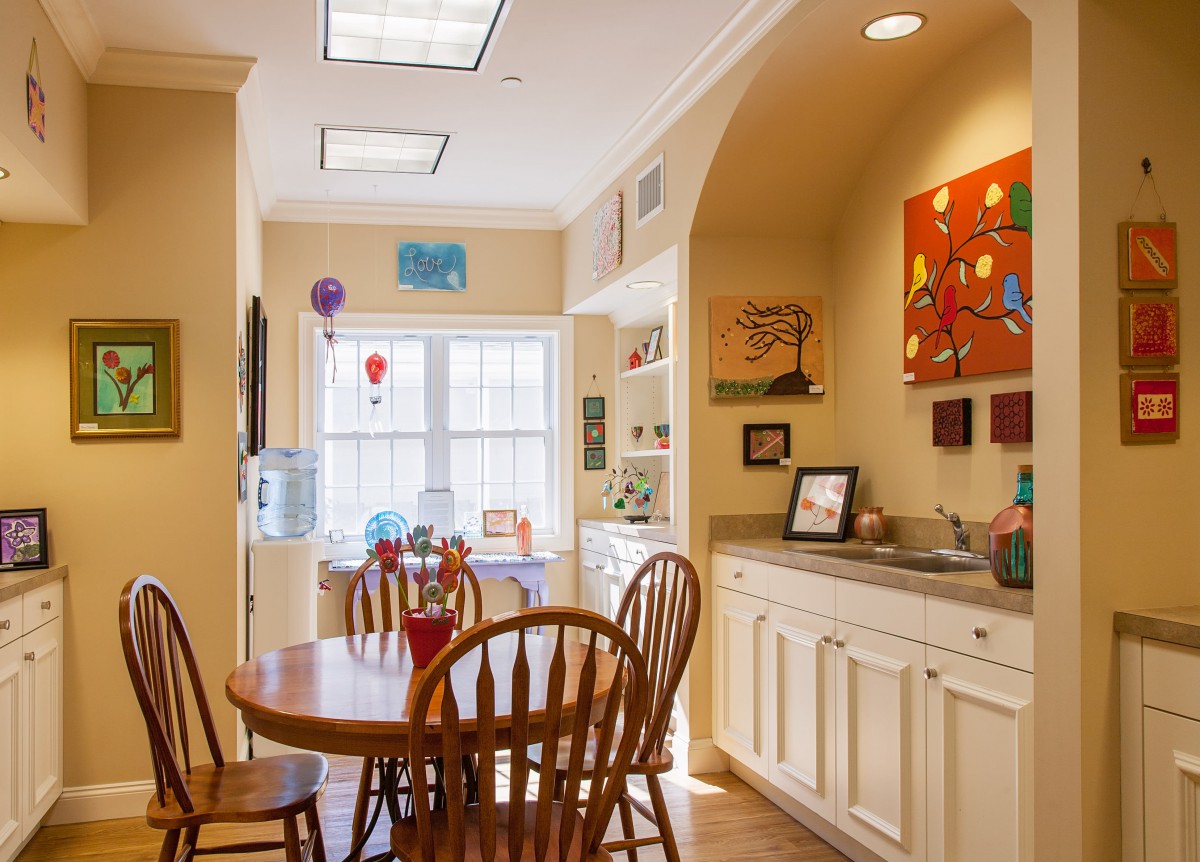 A cozy kitchen dining area with a table and chairs, adorned with colorful artwork and bathed in natural light.