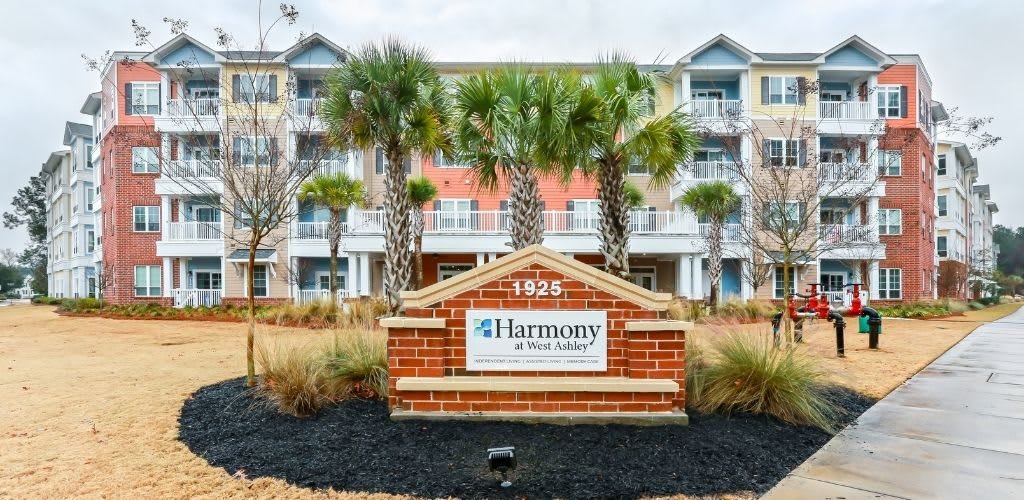 A residential complex with a Harmony at West Ashley sign and palm trees in front.
