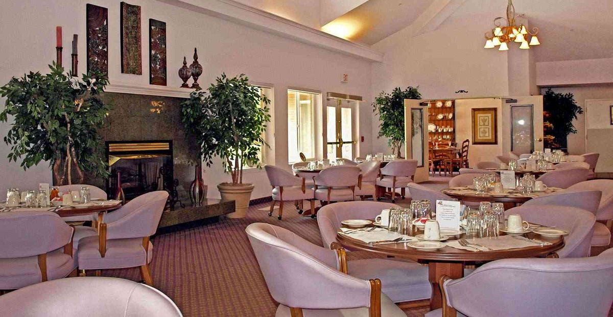 A cozy dining room with elegant decor, featuring tables and chairs arranged around a fireplace.