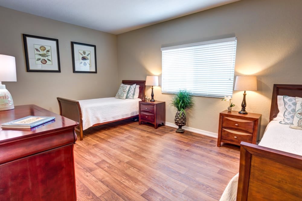 A tidy bedroom with hardwood floors, featuring a single bed, two bedside tables with lamps, and a window letting in natural light.