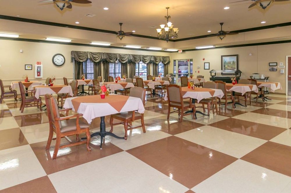 An elegantly decorated dining area featuring multiple tables and chairs, illuminated by chandeliers.