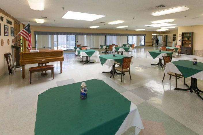 A spacious dining area with neatly arranged tables and chairs, featuring a piano in the corner.