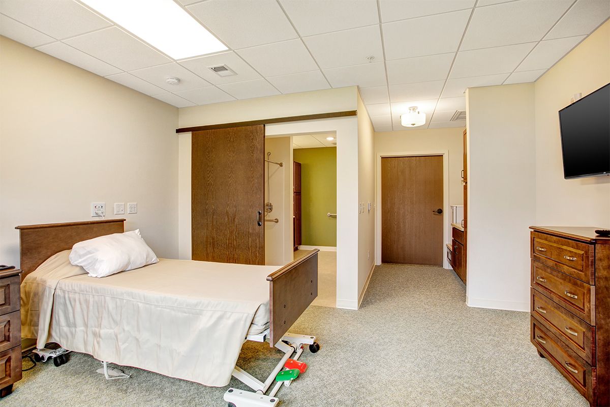 A hospital room with a bed and sliding door inside a medical facility.