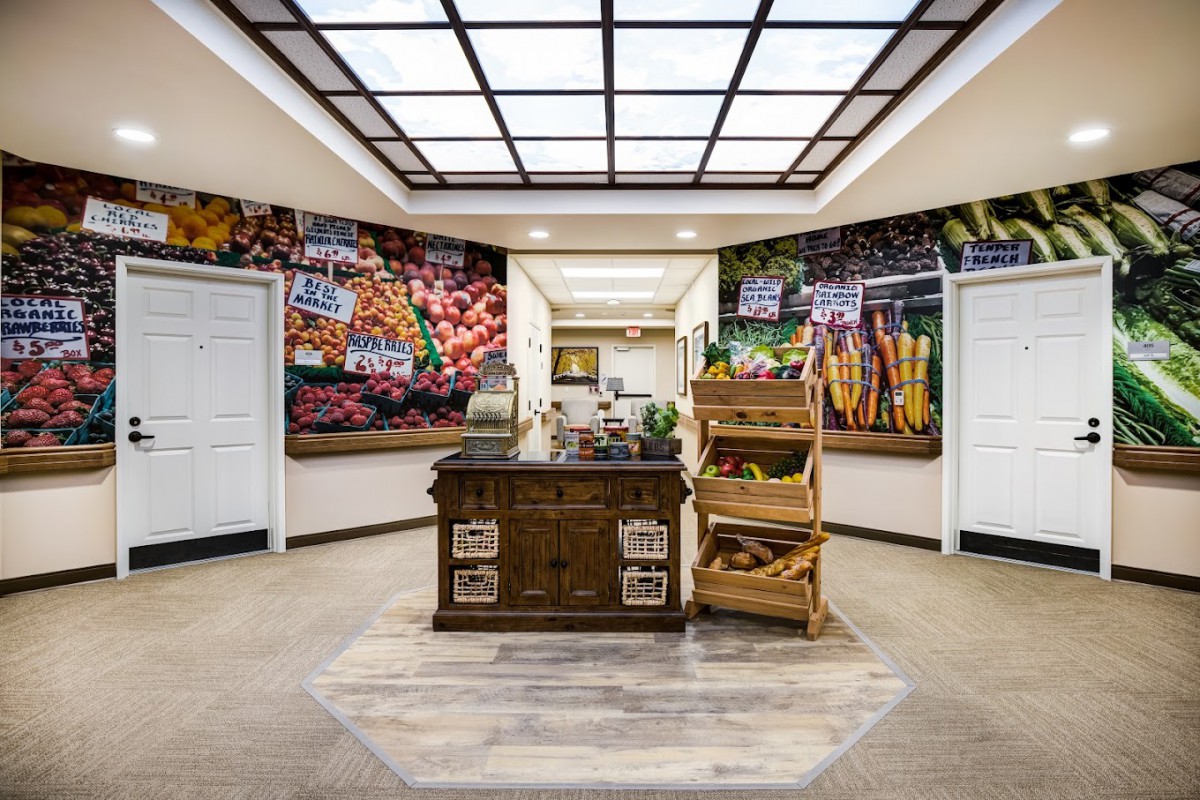 A small grocery store interior with a central counter, surrounded by vibrant displays of fruits and vegetables.