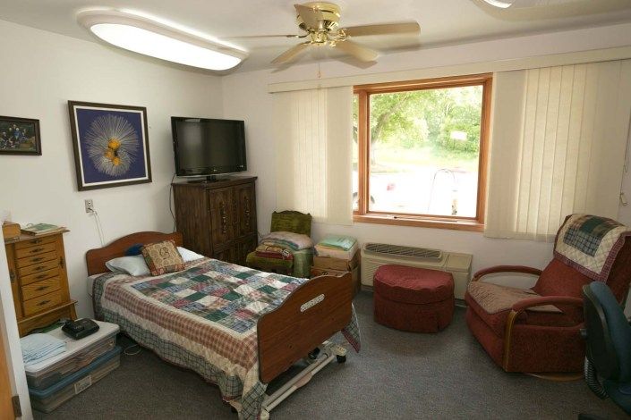 A cozy room with a hospital bed, TV, and a large window letting in natural light.