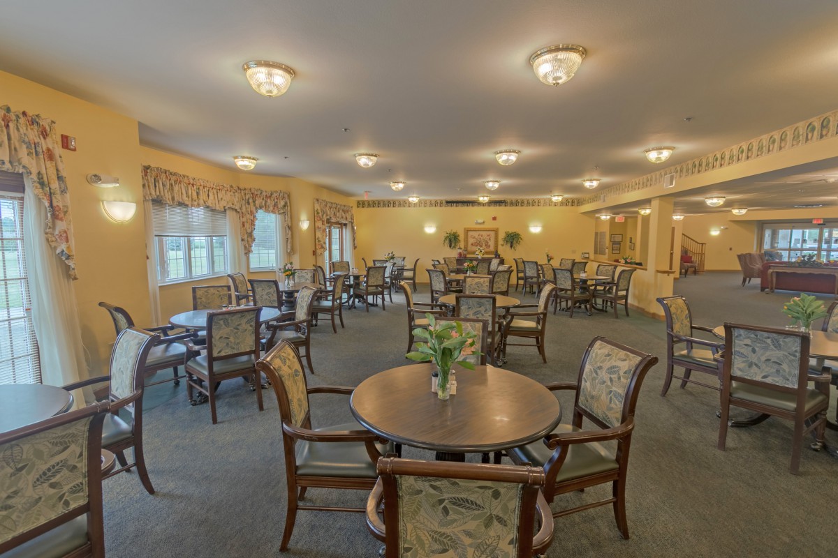 A spacious dining room with multiple tables and chairs, elegantly lit by ceiling lights.