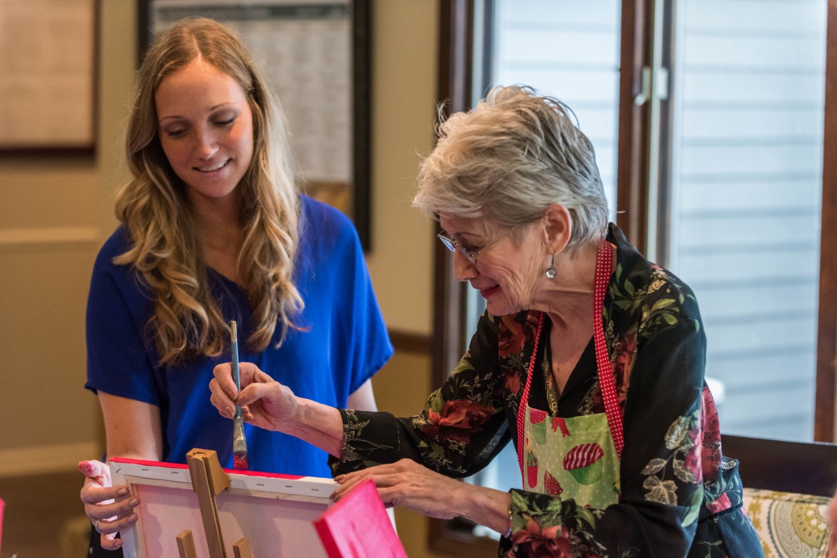 An elderly woman and a younger woman engaging in a painting activity together.