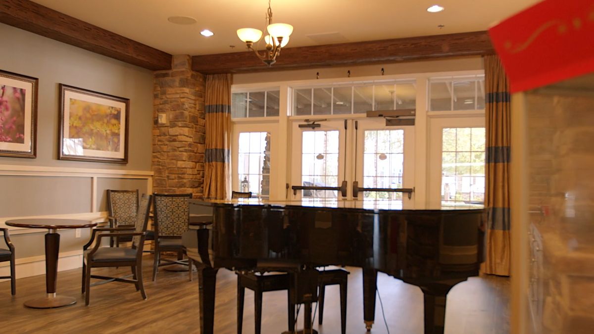 A cozy music room featuring a grand piano with wooden flooring and elegant chandeliers.