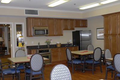 A modern kitchen and dining area featuring wooden cabinets, a refrigerator, microwave, tables, and chairs.