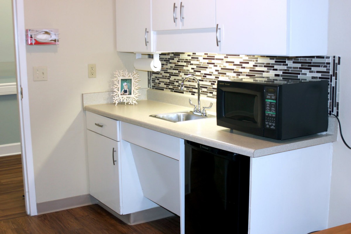 A small kitchen area with a microwave, sink, and cabinets.