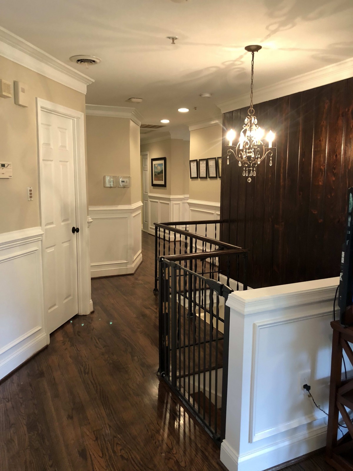 A well-lit hallway with wooden flooring, featuring a chandelier and decorative wall paneling.
