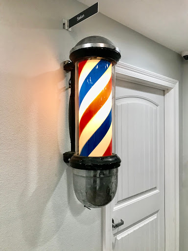 A classic barber pole with red, white, and blue stripes illuminated in a barbershop setting.