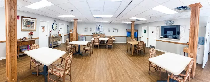 An empty dining area with wooden flooring, featuring tables and chairs arranged in a well-lit room.