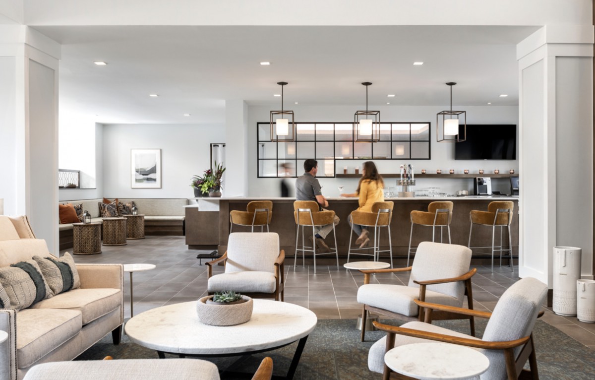 A modern lounge area with comfortable seating and a bar, featuring two people sitting at the counter.