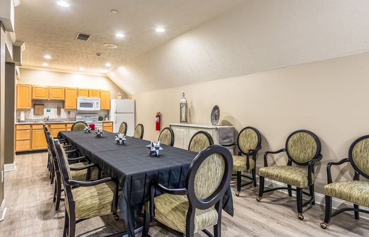 A conference room setup with a long meeting table and chairs, adjacent to a kitchen area.