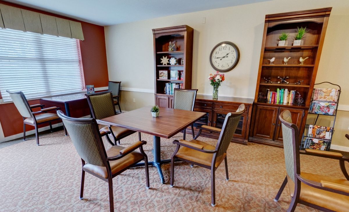 A cozy living room with a wooden table and chairs, flanked by bookshelves and adorned with a wall clock.
