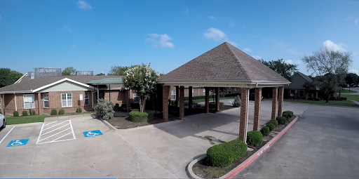 A view of a building with a canopy, surrounded by greenery under a clear blue sky.