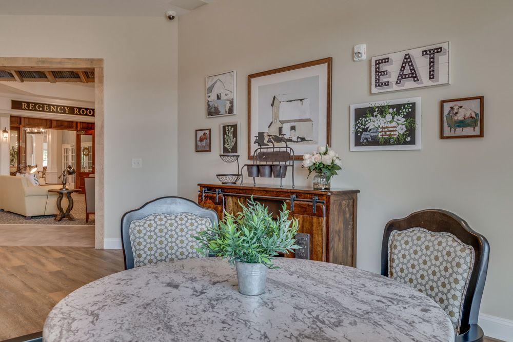 A cozy dining room featuring a round table with upholstered chairs, decorated with plants and framed artwork.