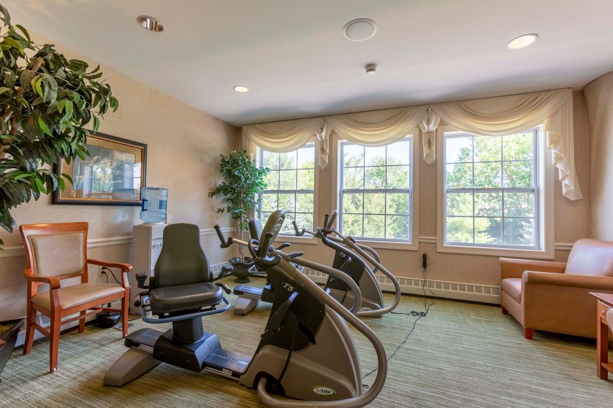 A fitness room with cardio machines and large windows allowing natural light.