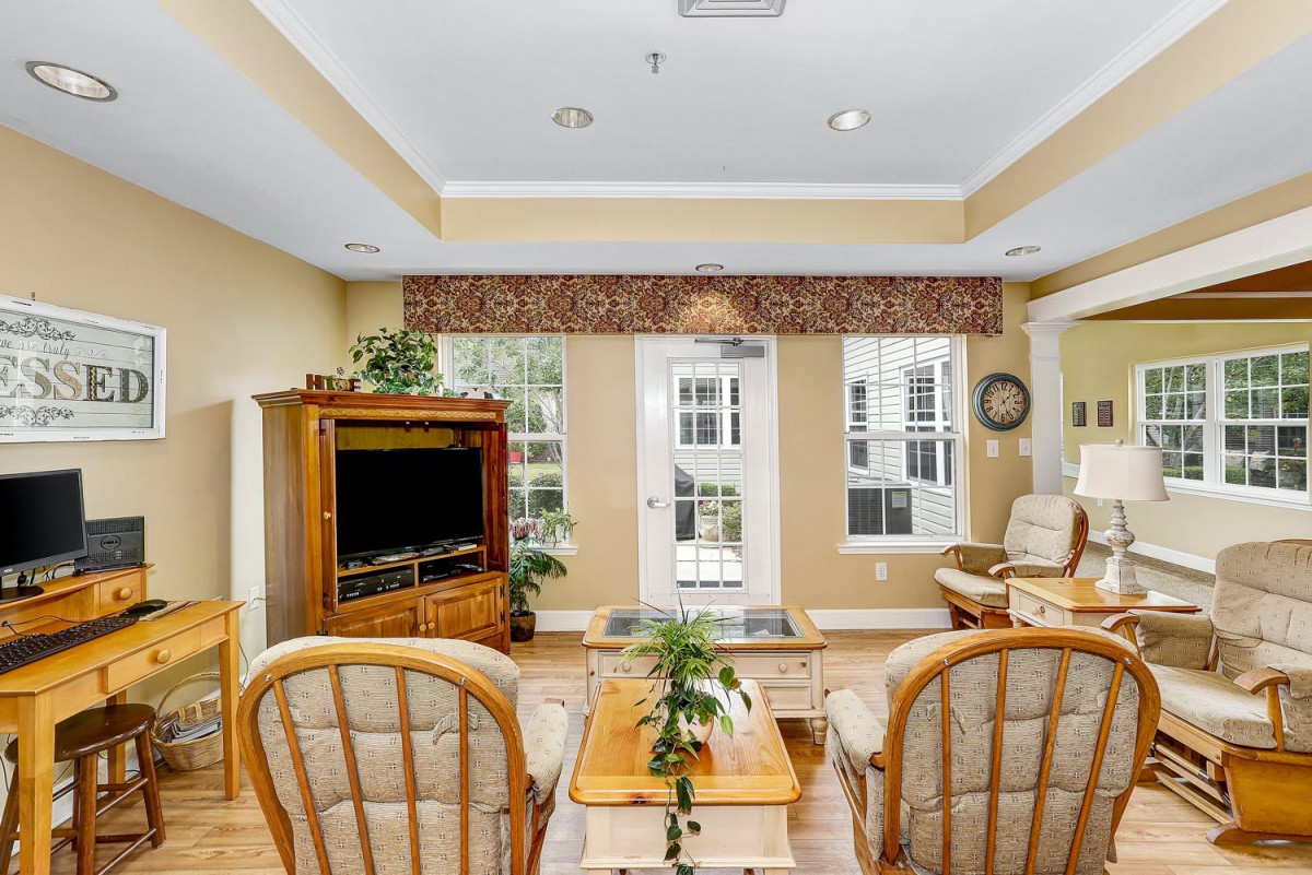 A cozy living room with wooden furniture, a TV, and large windows that let in natural light.