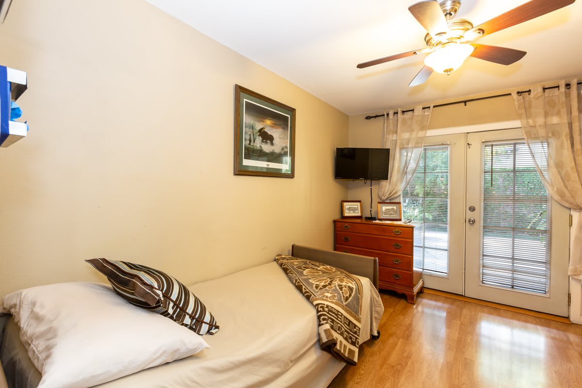 A cozy bedroom featuring a single bed, television, and a glass door leading outside.