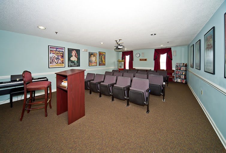 A small lecture room with rows of chairs and a podium, decorated with paintings.