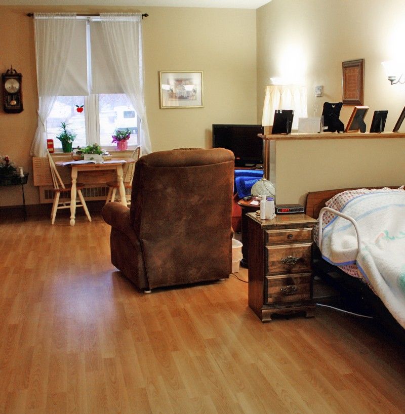 A cozy bedroom with an armchair, nightstand, and a small dining area.