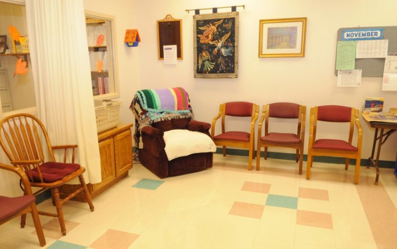 A cozy waiting room with chairs, a colorful blanket on an armchair, and artwork on the walls.