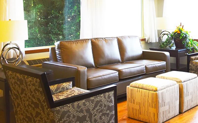 A cozy living room with a leather sofa, patterned armchair, and ottoman near a large window.