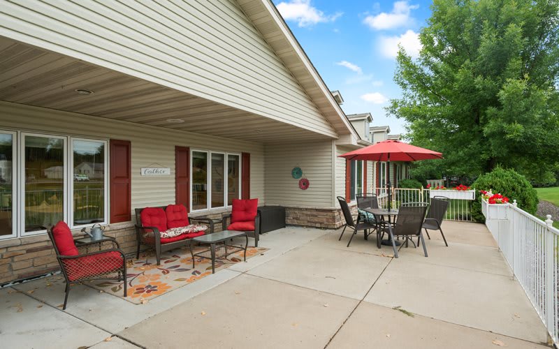 A cozy patio with red-cushioned seating and an umbrella-covered table, perfect for enjoying a sunny day.