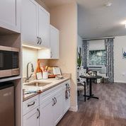 A modern, compact kitchen in an apartment with white cabinets and wood flooring.