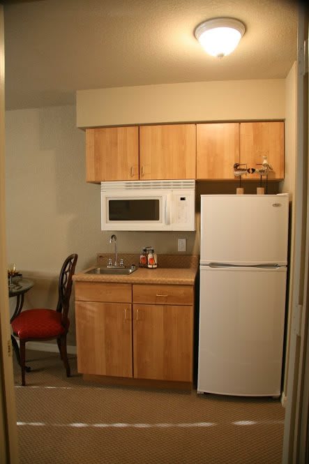 A compact kitchen area with wooden cabinets, a microwave, refrigerator, and small sink.