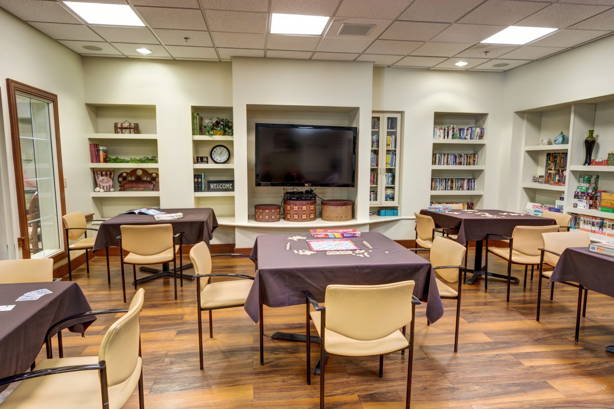A community room with tables, chairs, a television, and bookshelves.