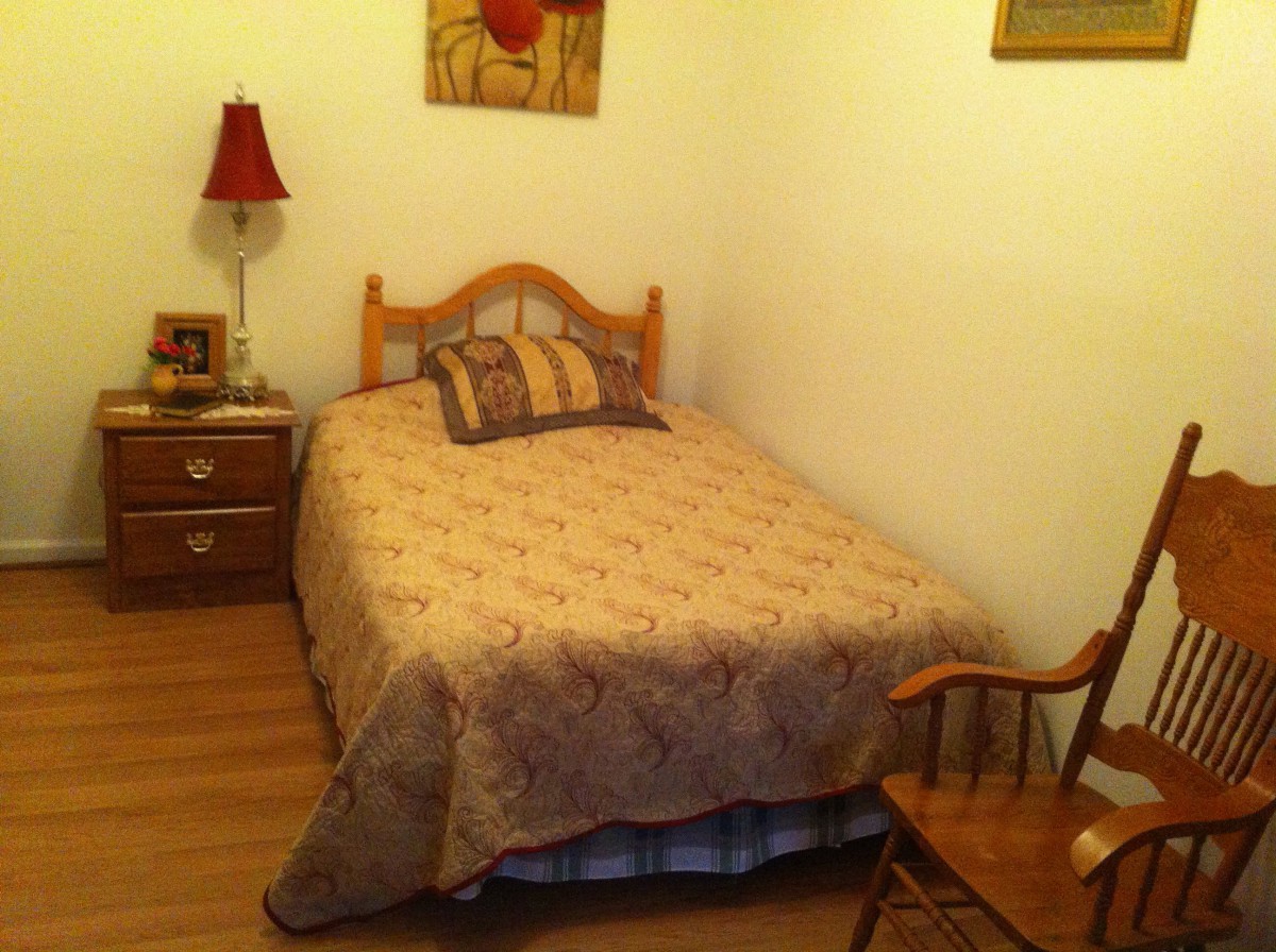 A cozy bedroom with a neatly made bed, nightstand with a lamp, and a rocking chair.