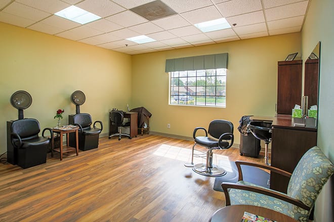 An empty hair salon with chairs and styling equipment, featuring a large window and wooden flooring.